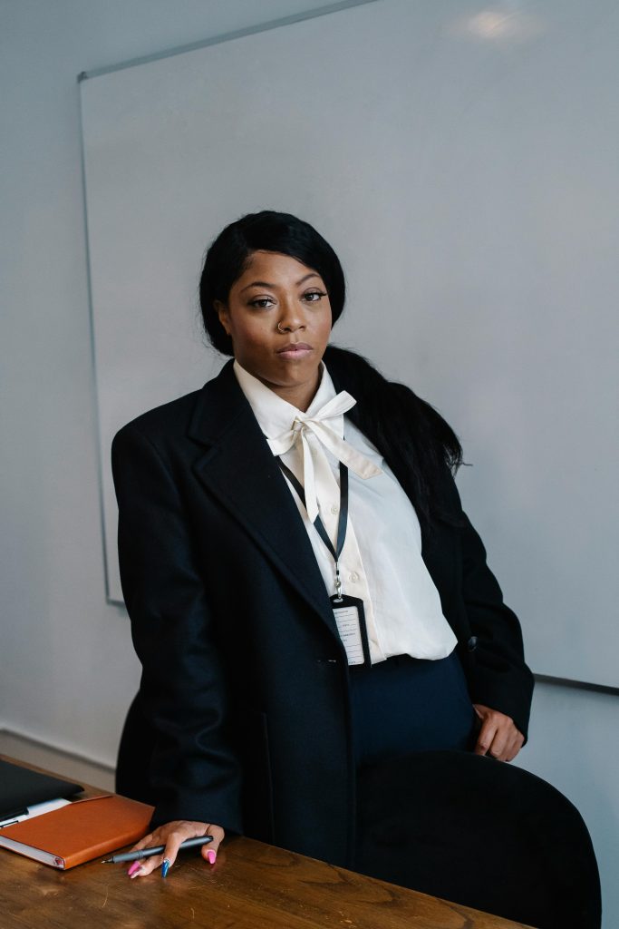 Serious African American female office worker in formal suit standing near table in modern workspace